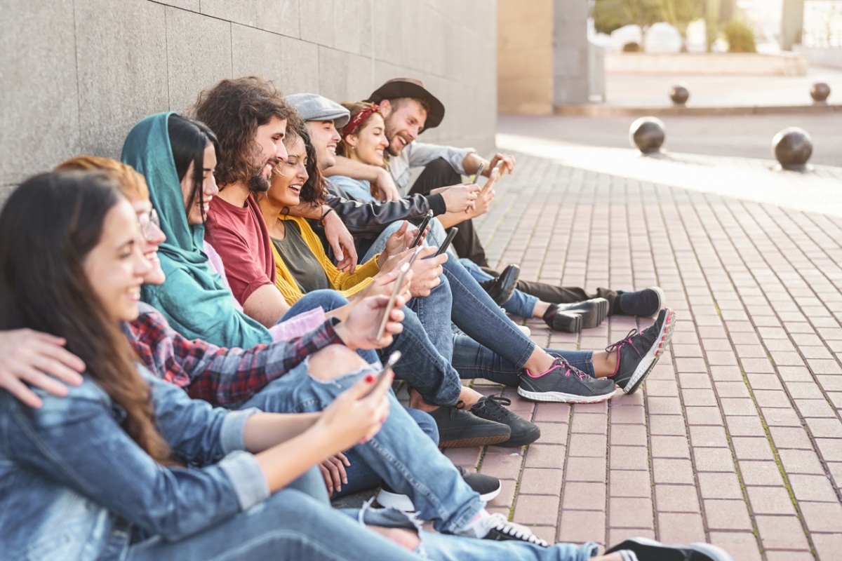 Junge Erwachsene sitzen mit Smartphones an einer Mauer
