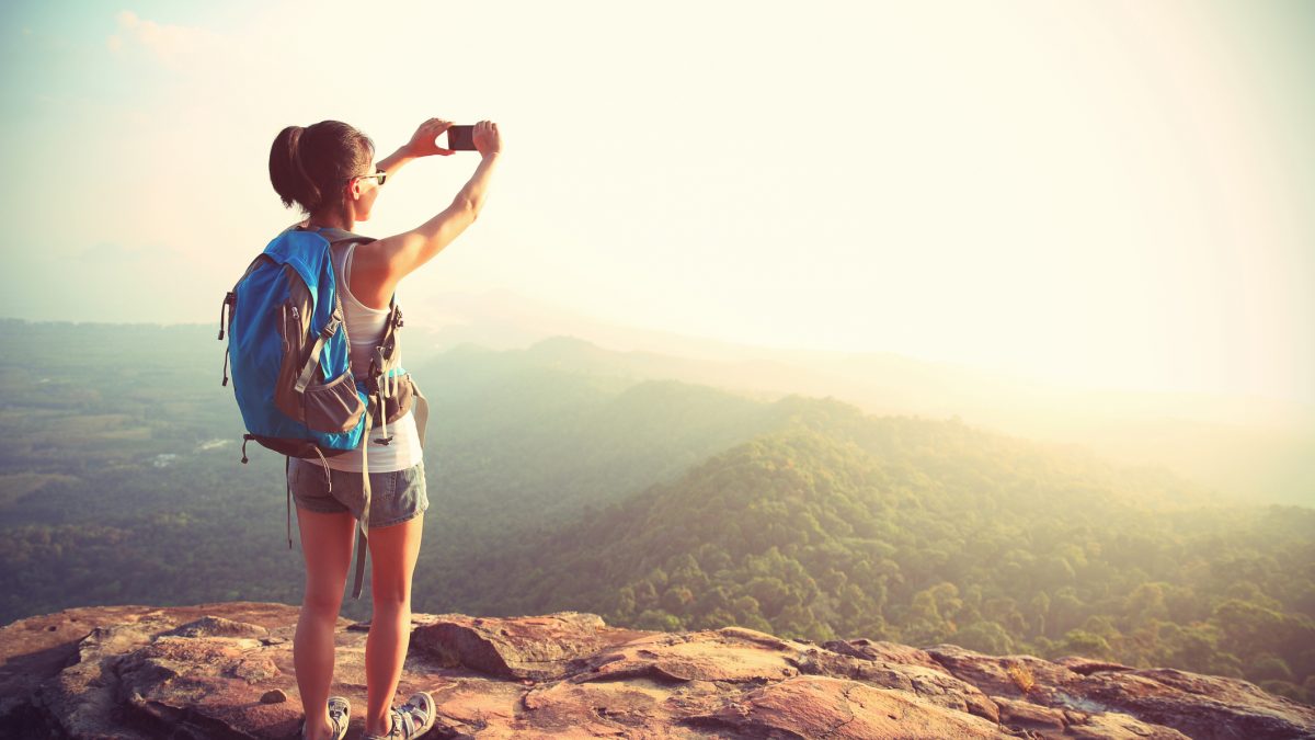 Eine Frau steht auf einem Berg und macht mt ihrem Smartphone ein Foto